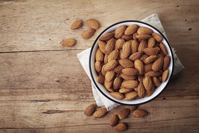 White bowl of almonds on wooden background