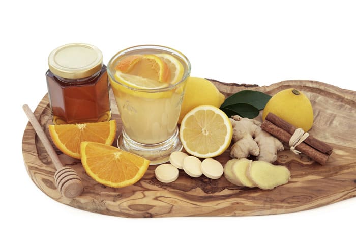 Cold and flu healing drink with vitamin c tablets, orange, lemon, ginger and cinnamon spice on olive wood board over white background.