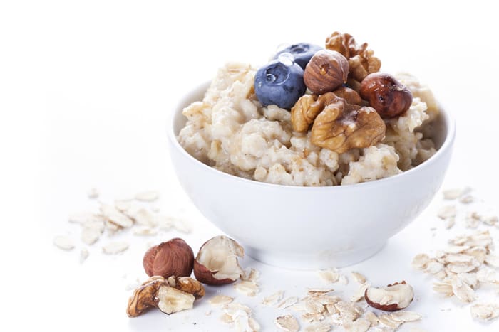 Oatmeal porridge in bowl topped with fresh blueberries, nuts and honey on white background