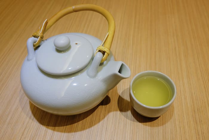 A cup of japanese green tea with teapot on wooden table